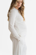 A pregnant woman wearing a matching white long-sleeve top and pants set, shown in profile against a clean white studio background.