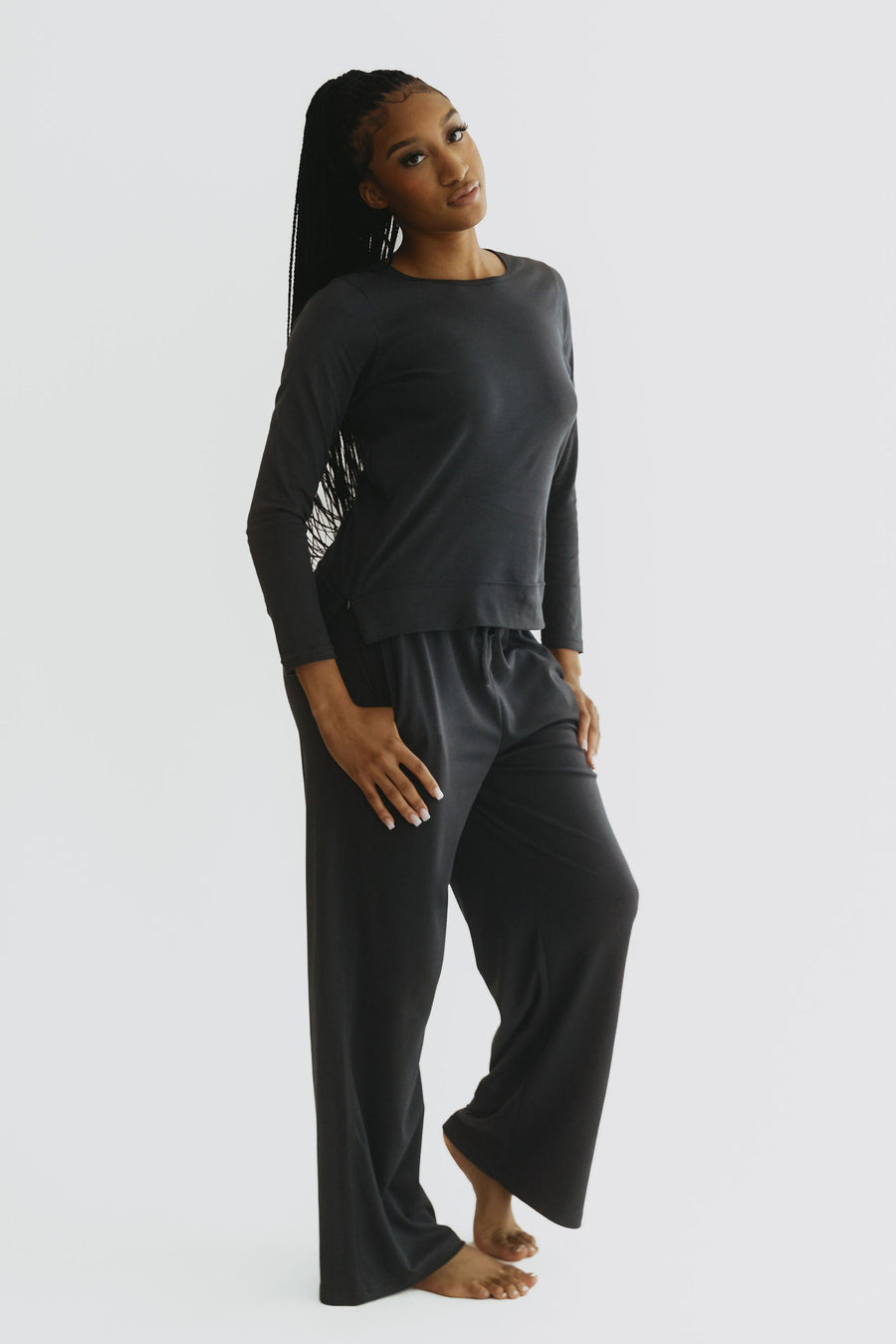 A woman modeling a dark gray two-piece loungewear set consisting of a long-sleeve top with a graphic print on the sleeve and matching wide-leg pants, shot against a plain light gray background. - Onyx
