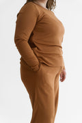 A person wearing a matching rust-brown knit lounge set with a long-sleeve top and pants, shown in side profile against a clean white studio background.
