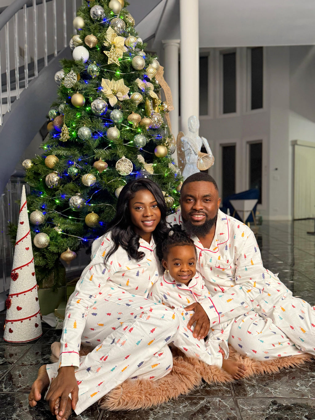 Family in matching pajamas sitting on a rug in front of a decorated Christmas tree.