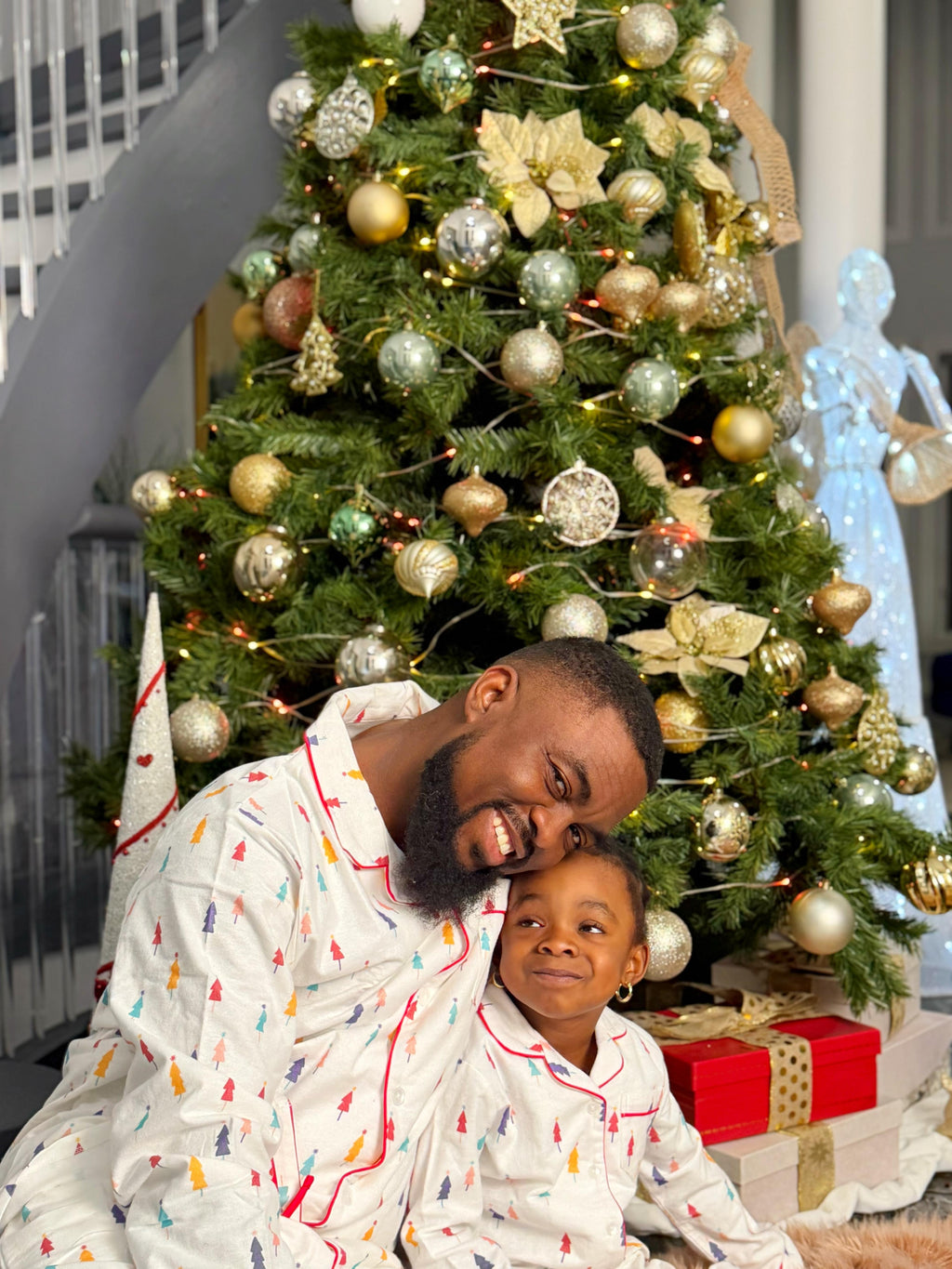 Man and child in pajamas sitting in front of a decorated Christmas tree.
